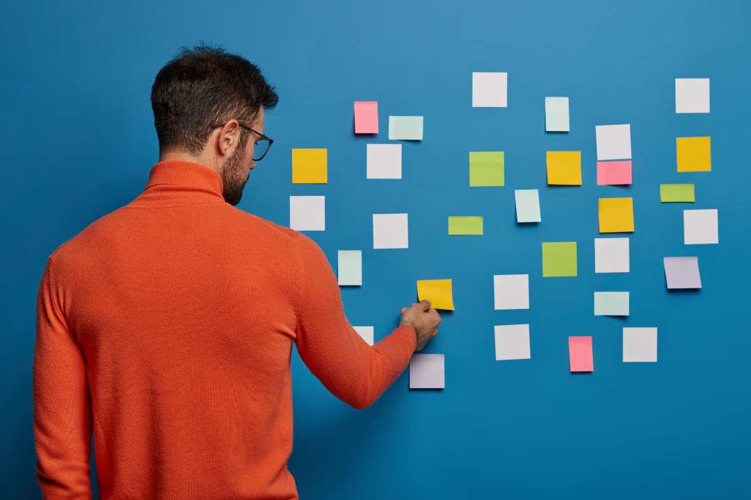 A person putting sticky notes on wall to manage task